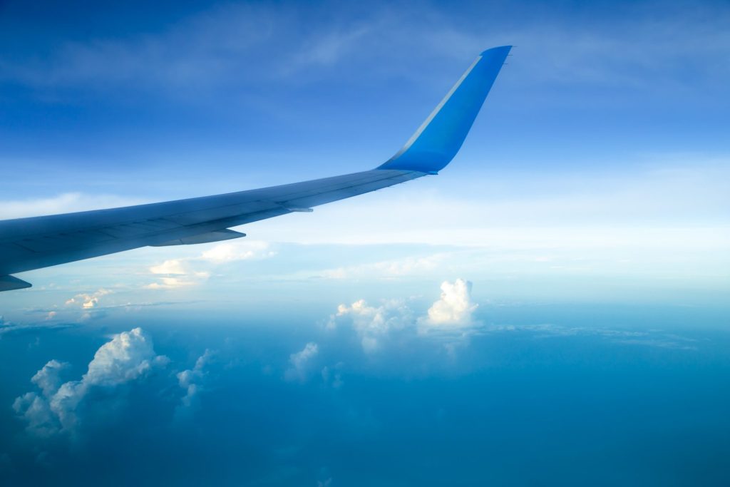 Airplane wing against blue sky with scattered clouds below