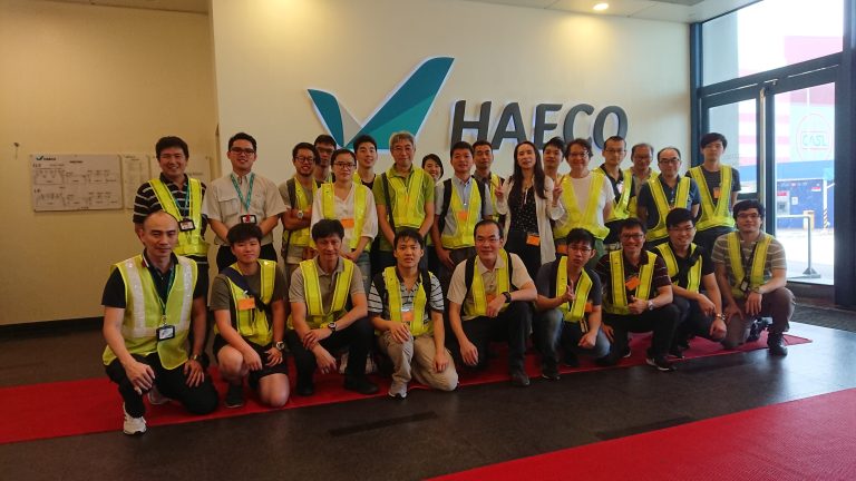 Group of people in safety vests posing for photo in front of HAECO logo