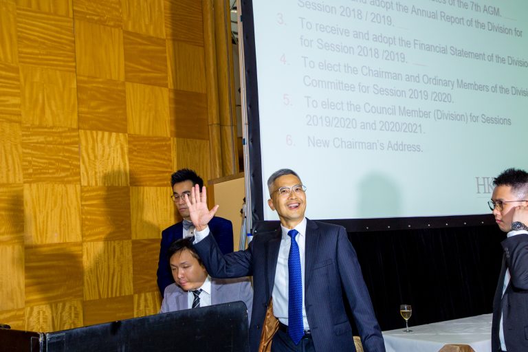 Man in suit waving at audience during business meeting with presentation screen behind.
