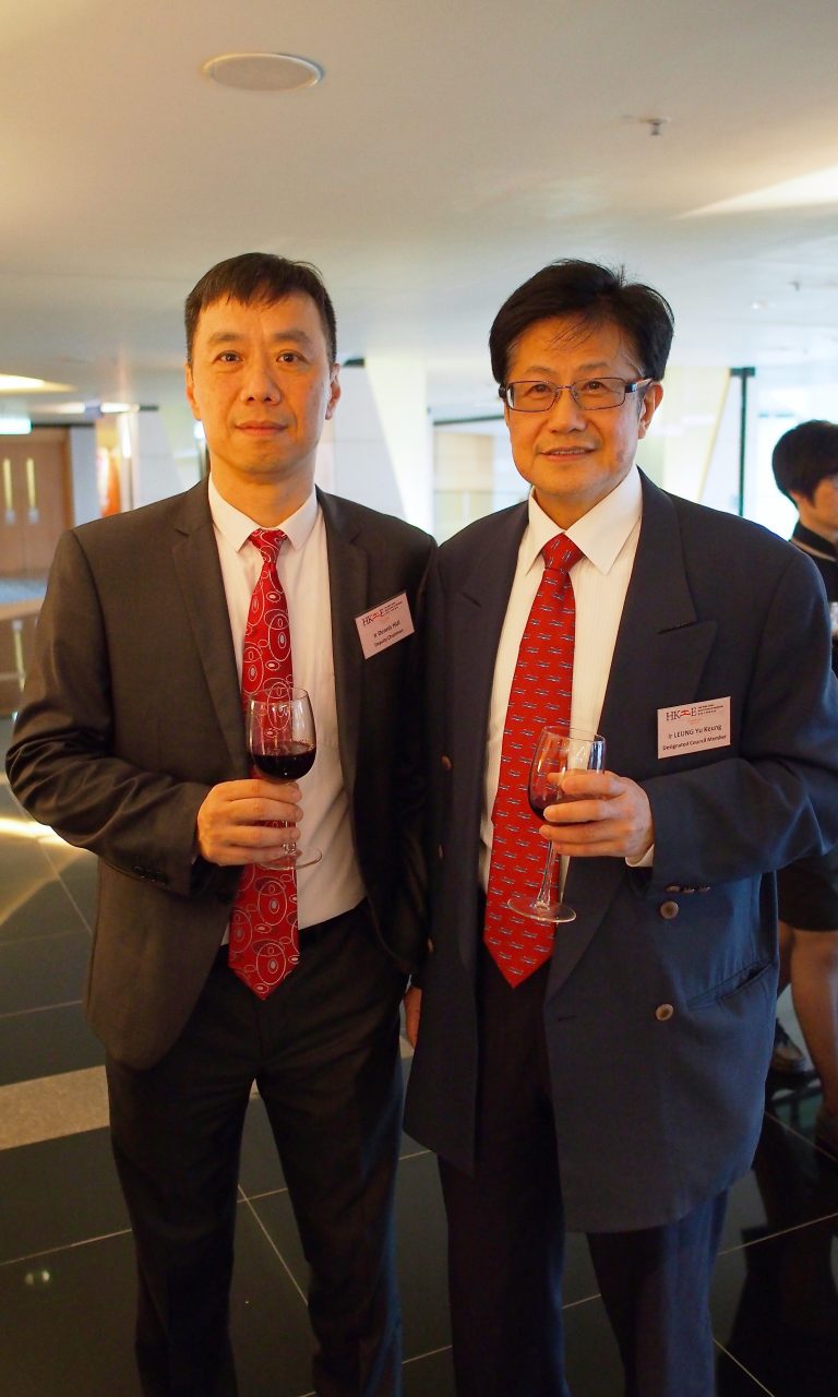 Two men in suits with name tags holding wine glasses at an event.