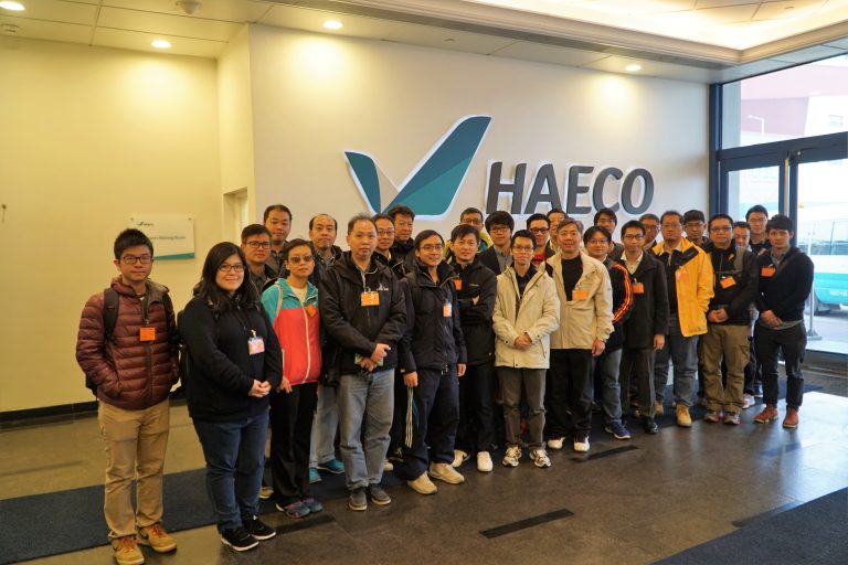 Group of people posing for photo in front of HAECO logo at company entrance
