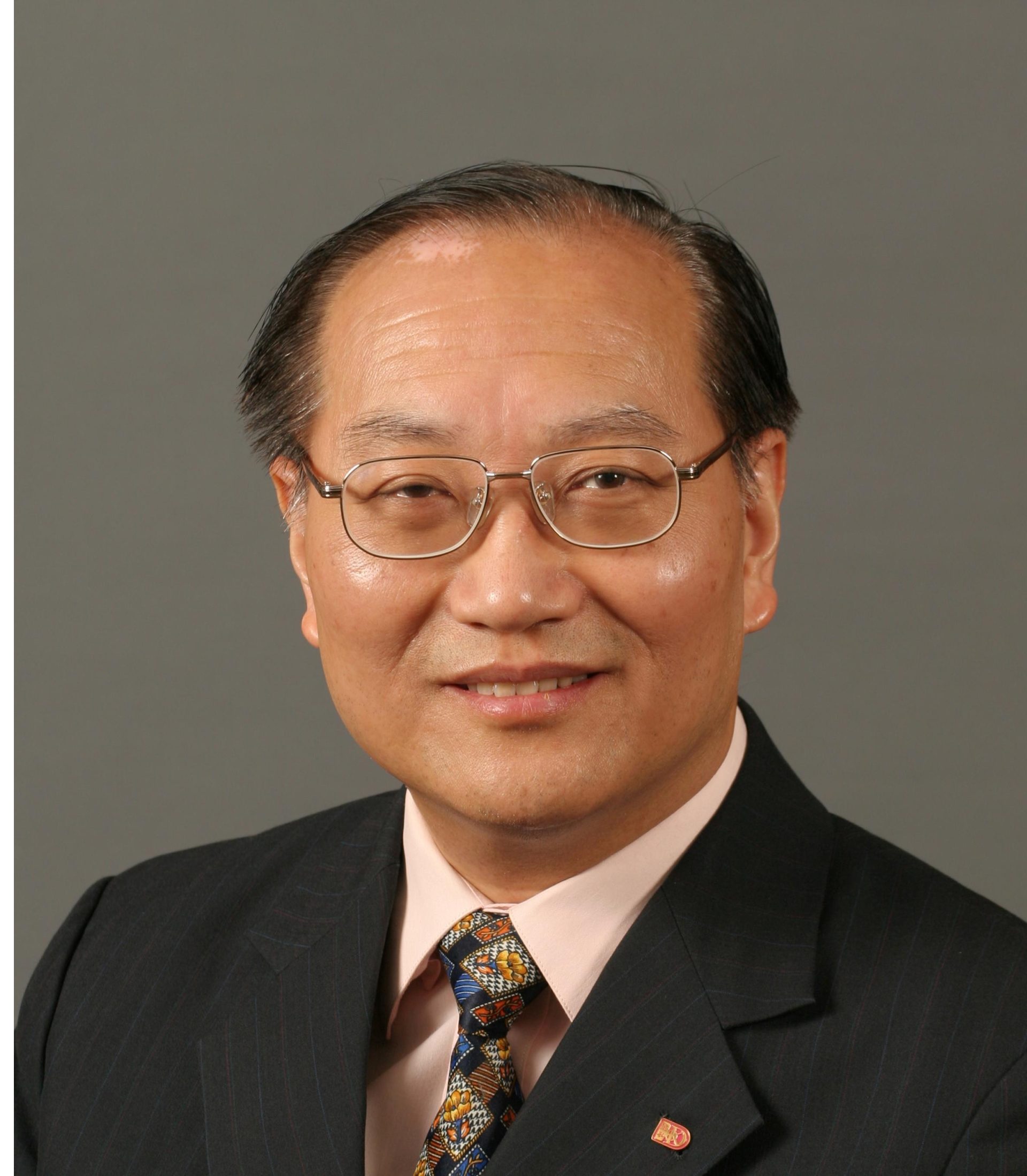 Portrait of John Mok wearing glasses, suit, and patterned tie.