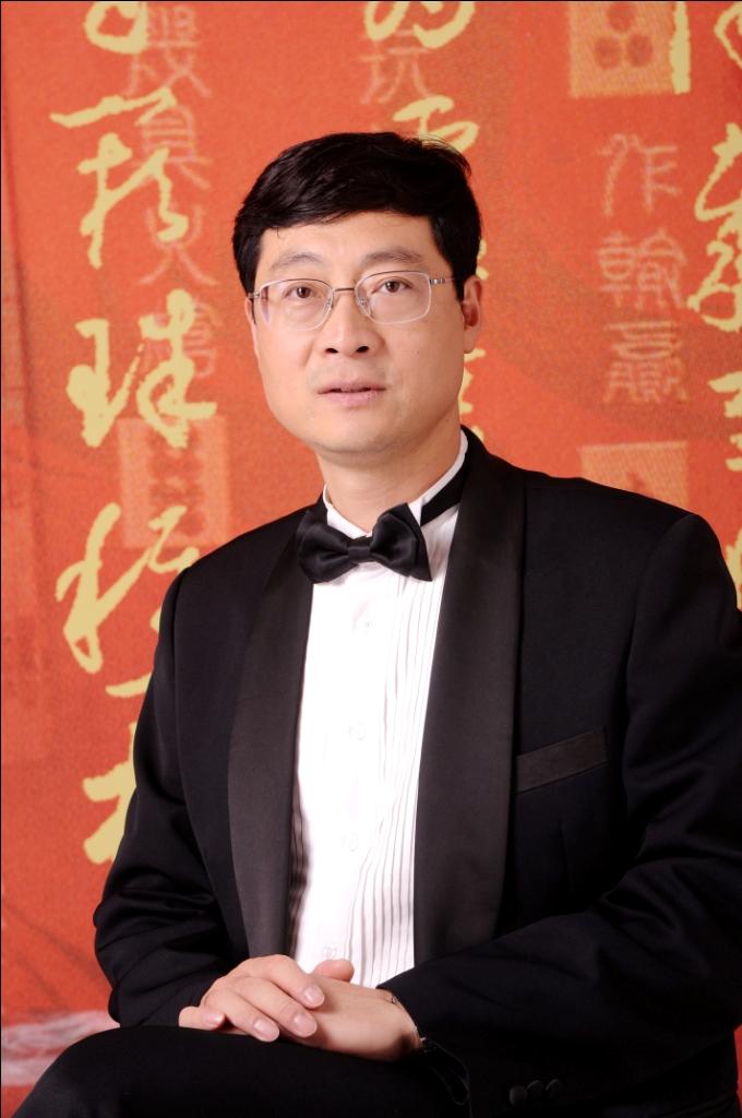 Man in tuxedo and bow tie posing against decorative red background with gold calligraphy.