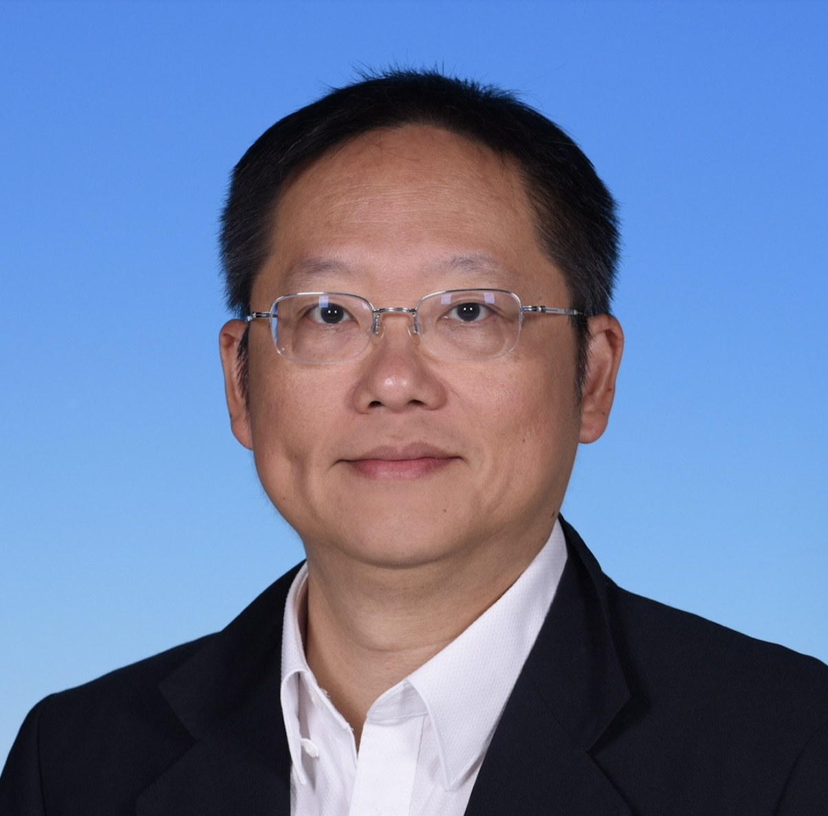 Headshot of a man with glasses wearing a suit and white shirt against a blue background.
