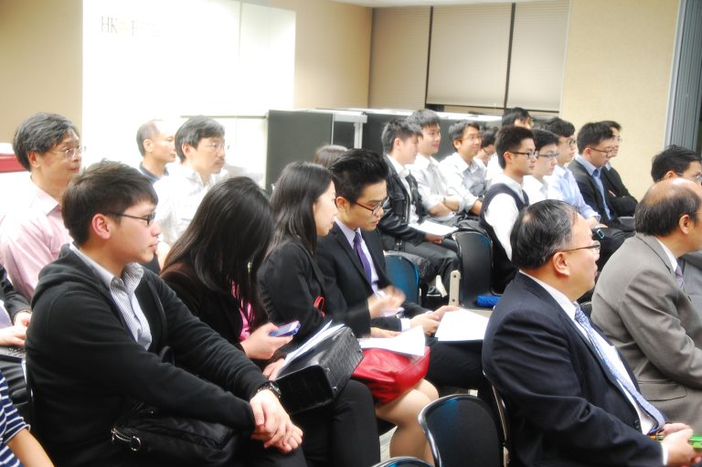 Audience seated in conference room, attentively listening to presentation.