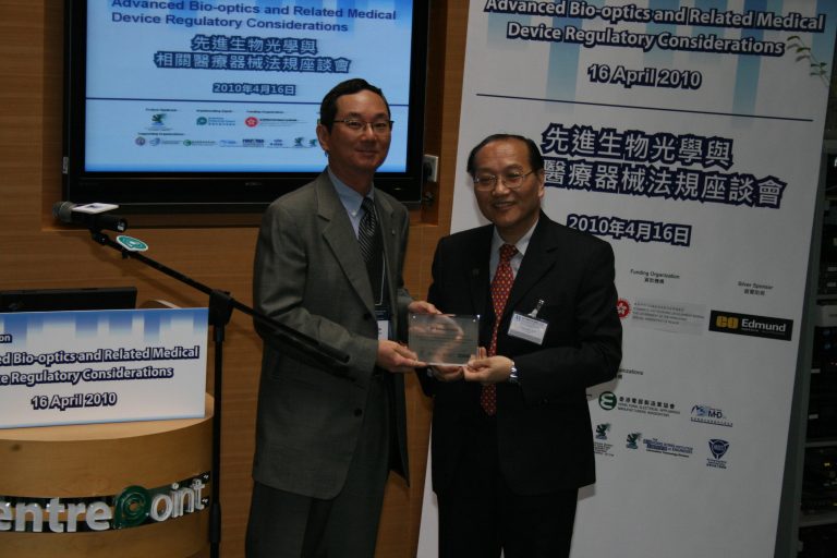 Two men in suits exchanging an award at a 2010 bio-optics regulatory conference.