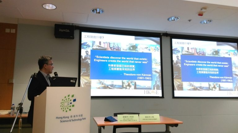 Man presenting at Hong Kong Science & Technology Parks with dual screens displaying engineering quote.
