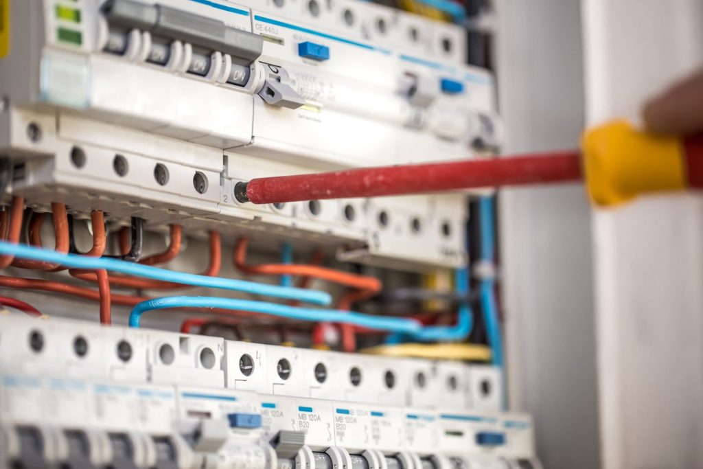 Electrician connecting wires in a circuit breaker panel with red and blue cables.