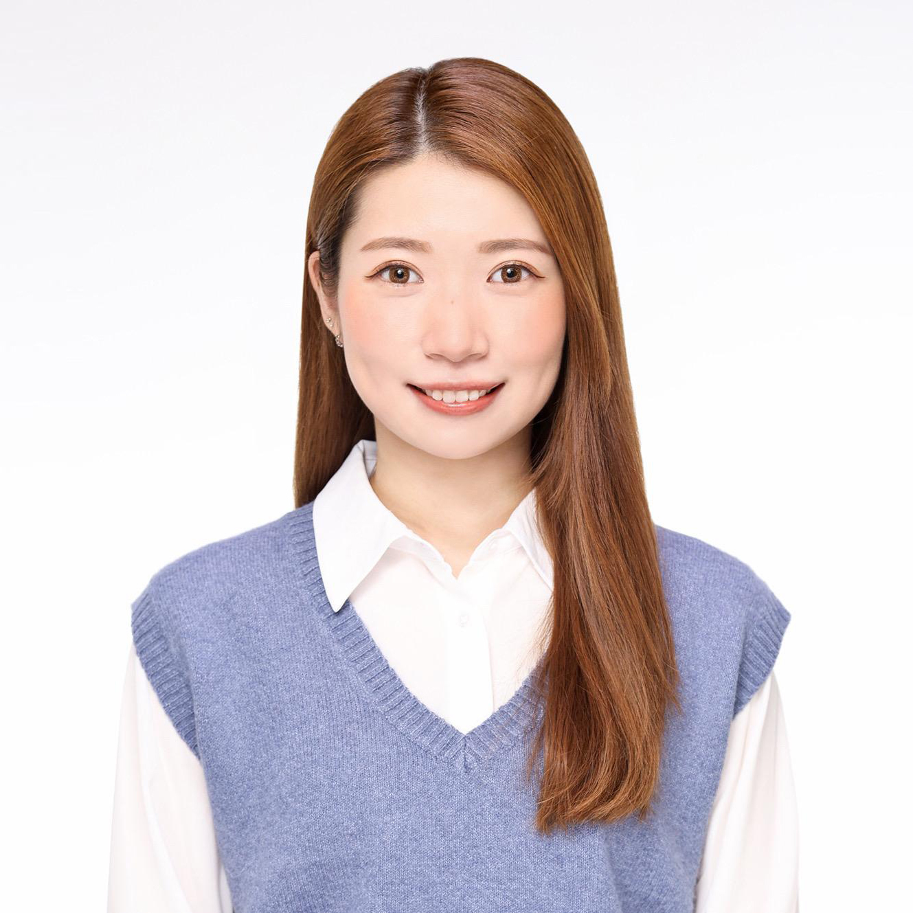 Portrait of a smiling woman with long brown hair wearing a blue vest over a white shirt.