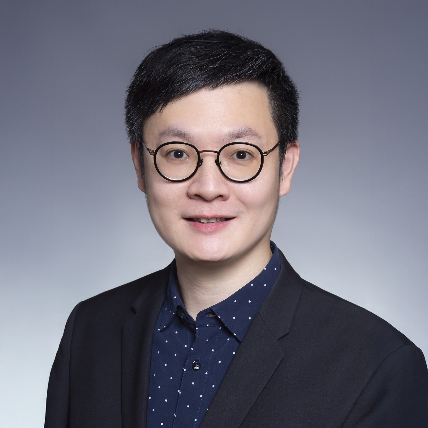 Man with glasses and dark suit smiling at camera