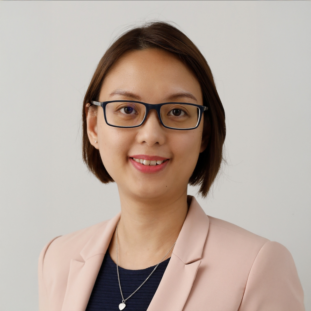 Professional headshot of a woman with glasses, smiling, wearing a pink blazer.