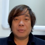 Portrait of a man with shoulder-length dark hair wearing a dark collared shirt.