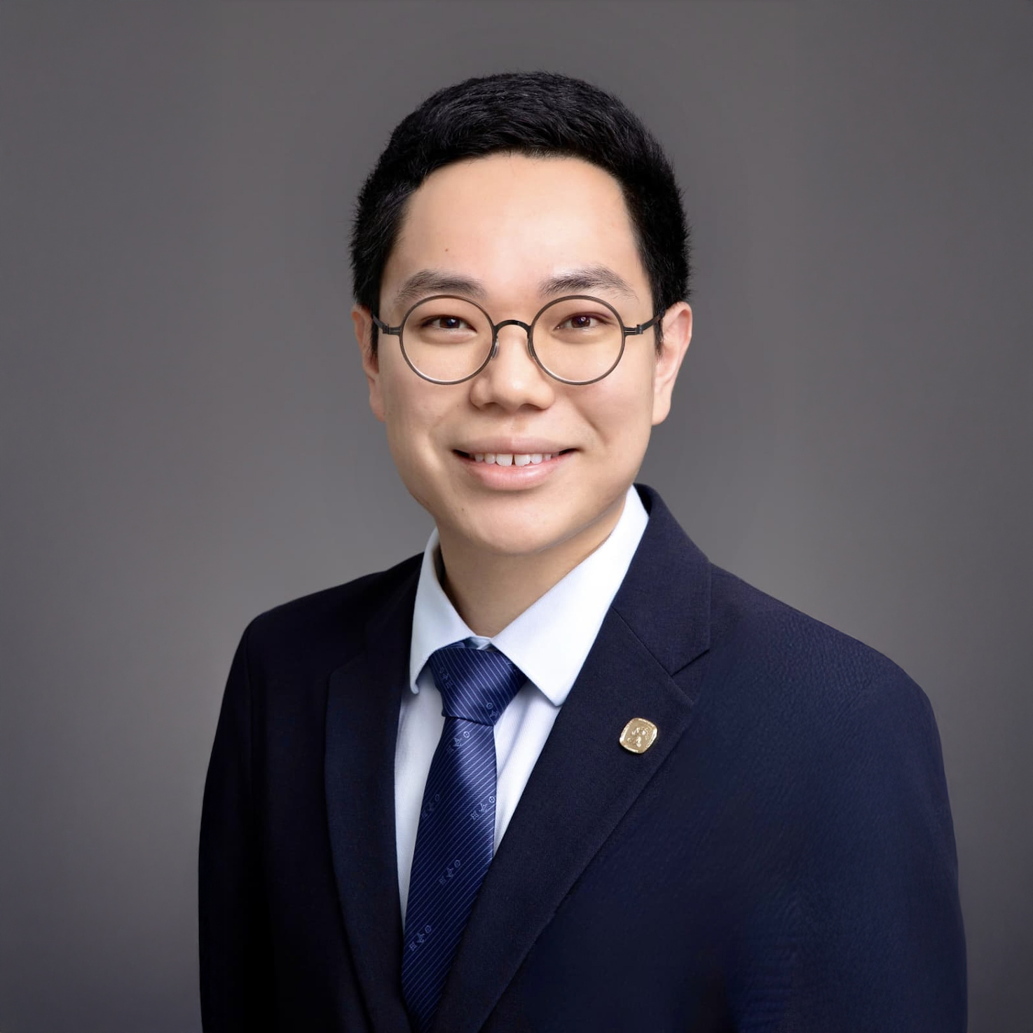 Professional headshot of a smiling man in glasses, suit, and tie.