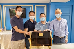 Four men wearing masks stand together, placing hands on a glass-topped display case.