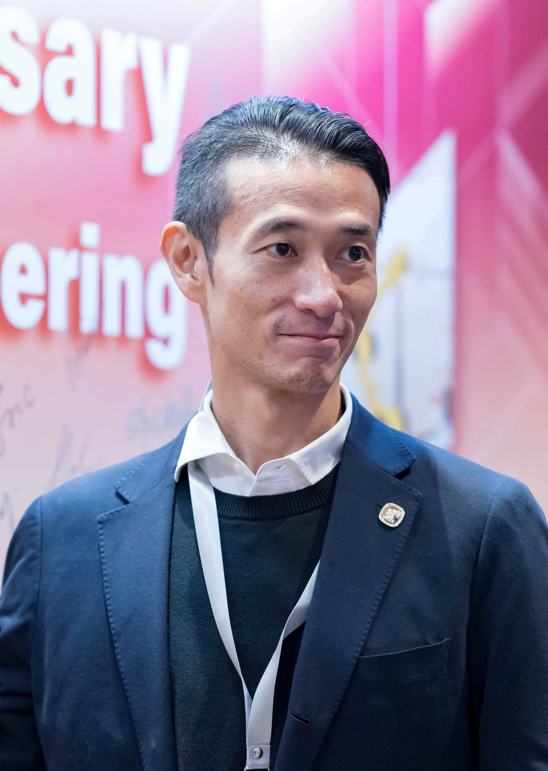 Man in suit with lanyard at event, smiling slightly