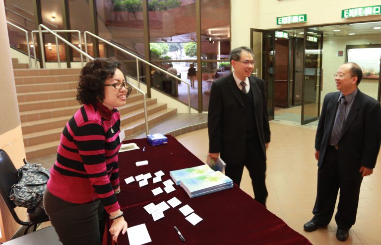 Three people interacting at an indoor event table with brochures and name tags.