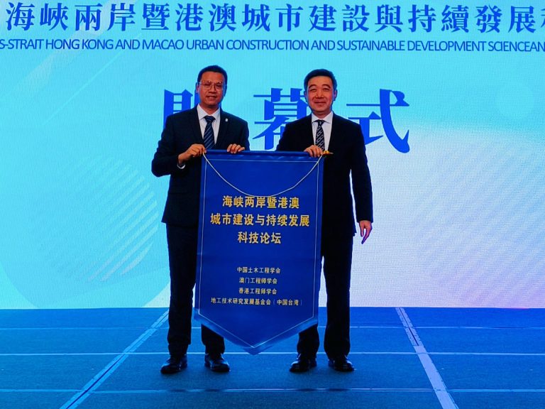 Two men in suits holding a blue banner at a forum on cross-strait urban development.