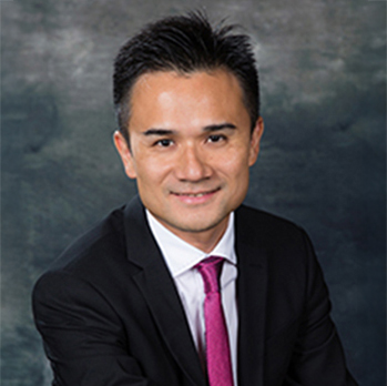 Professional headshot of a smiling man in suit and magenta tie