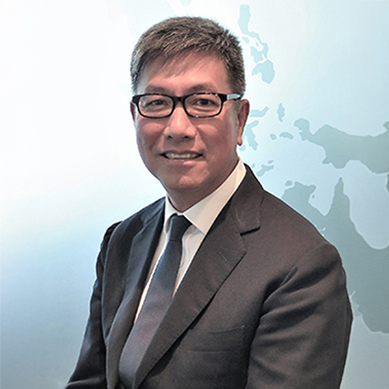 Man in suit and glasses smiling, with world map background