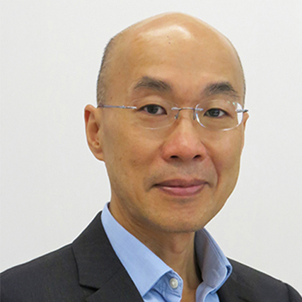 Portrait of a bald Asian man wearing glasses and a suit jacket over a blue shirt.