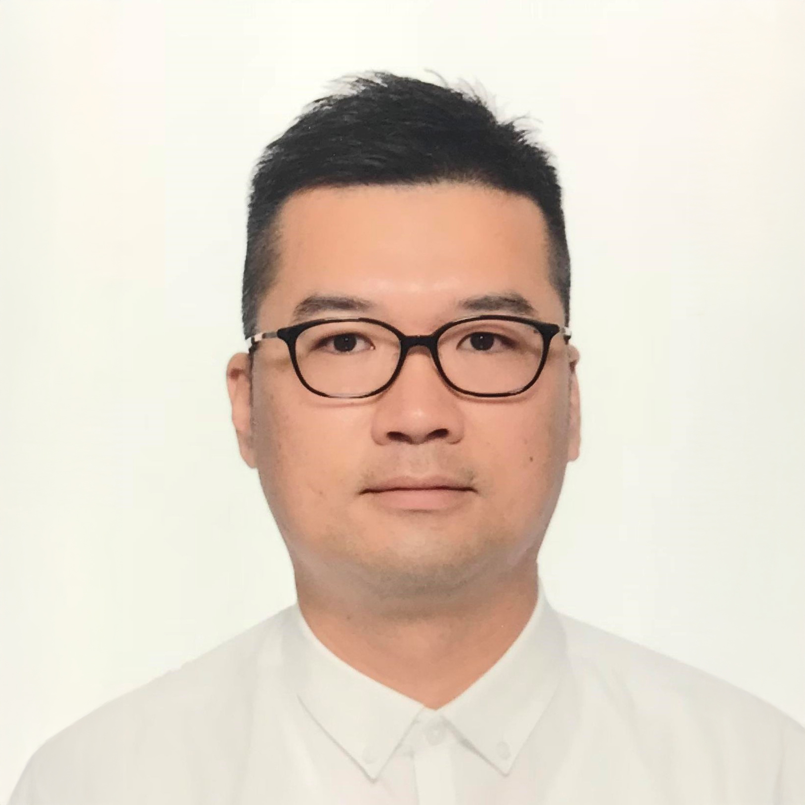 Man with dark hair and glasses wearing a white collared shirt.