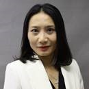 Portrait of a woman with dark hair wearing a white blazer against a gray background.