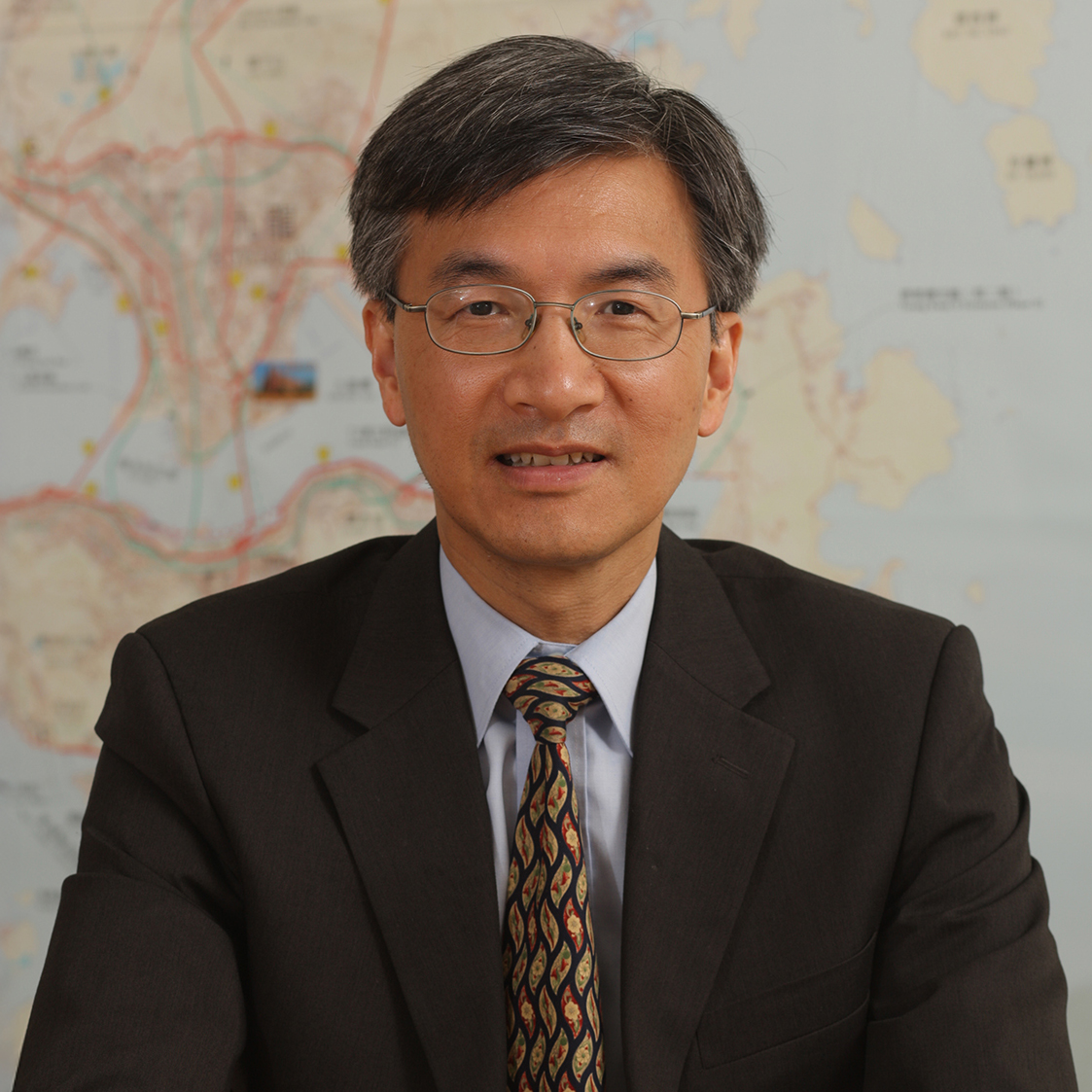 Man in suit and glasses, standing before a map background.