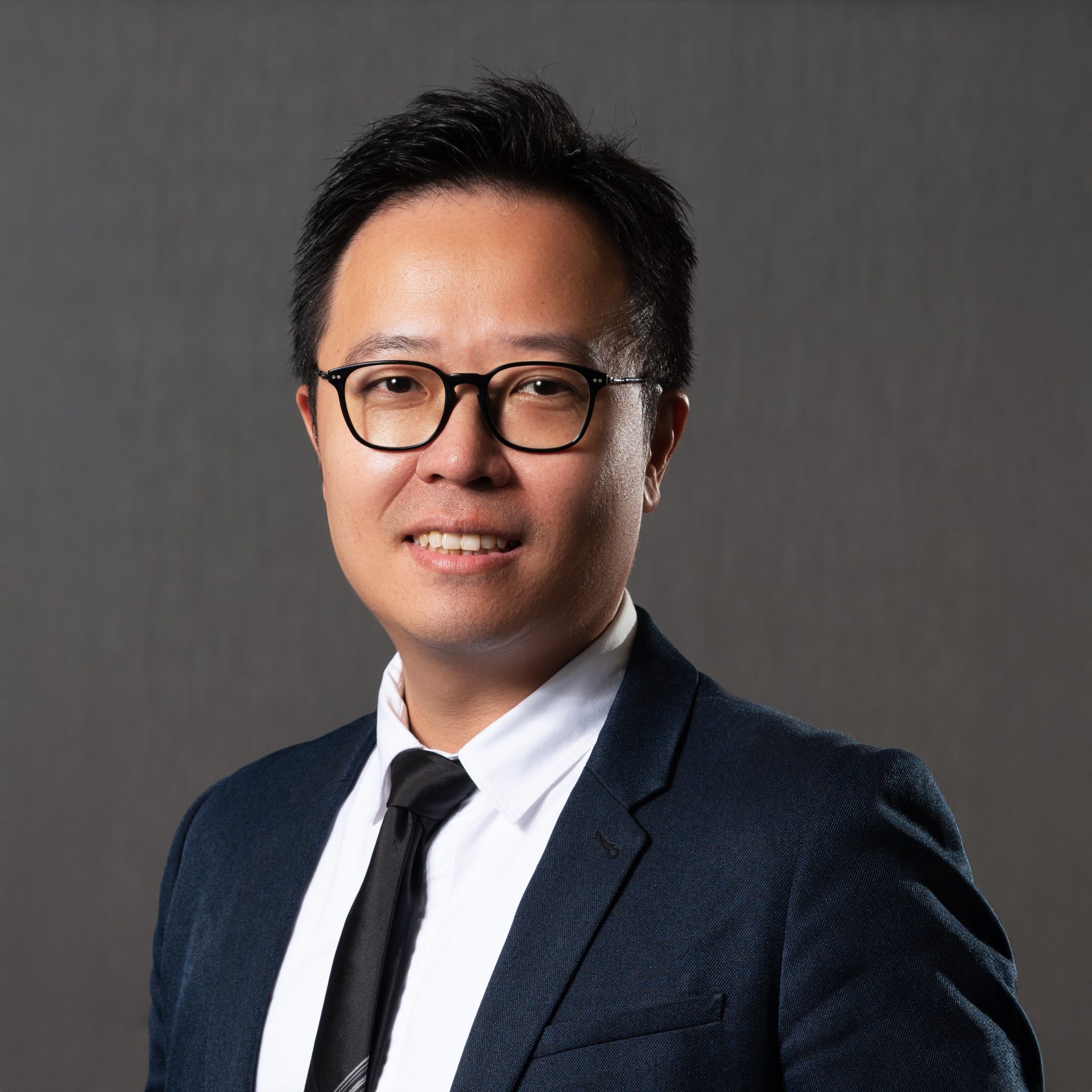 Professional headshot of a man wearing glasses, a suit, and tie.