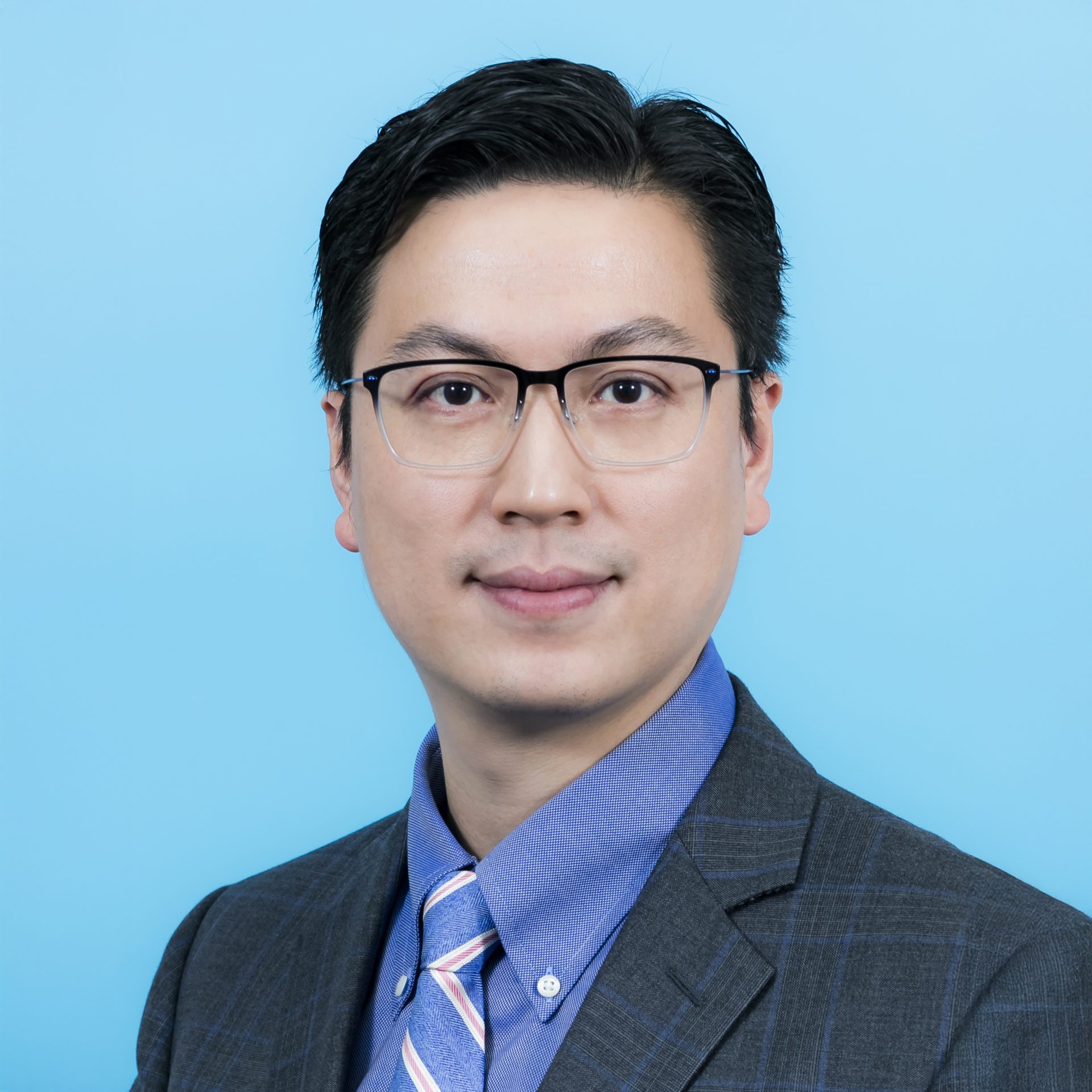 Headshot of a man with glasses wearing a suit and tie against a blue background.