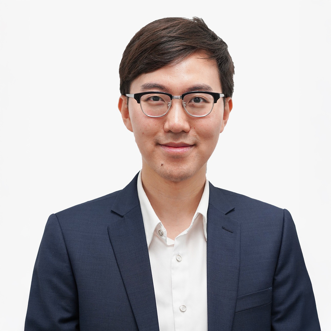 Man with glasses wearing a navy blazer and white shirt, smiling at the camera.