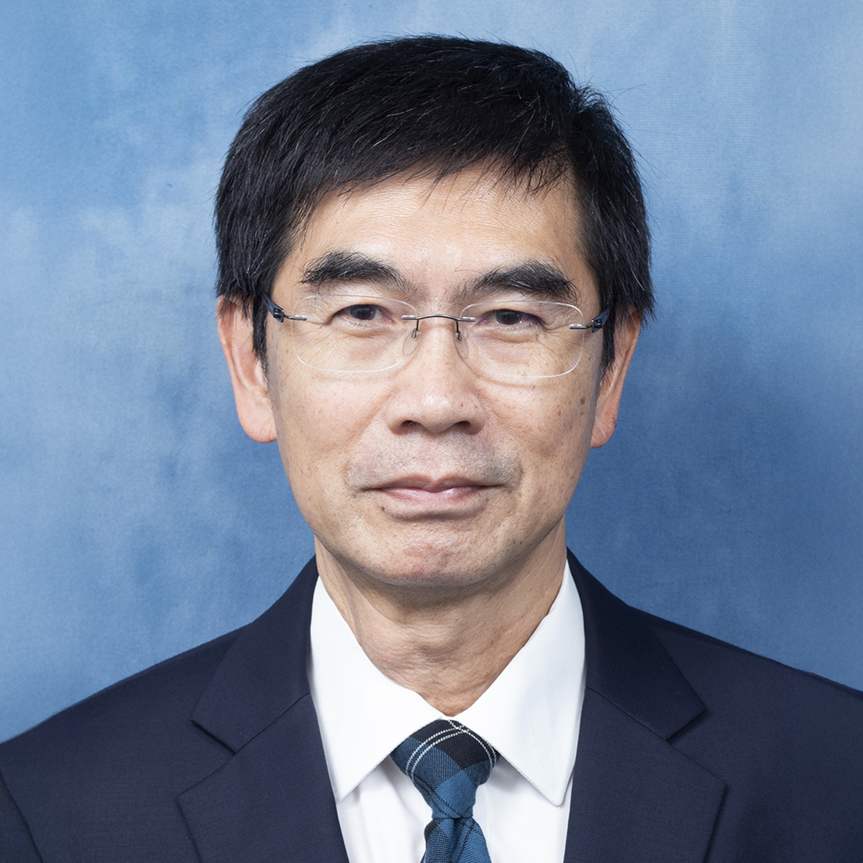 Portrait of a man with glasses wearing a suit and tie against a blue background.
