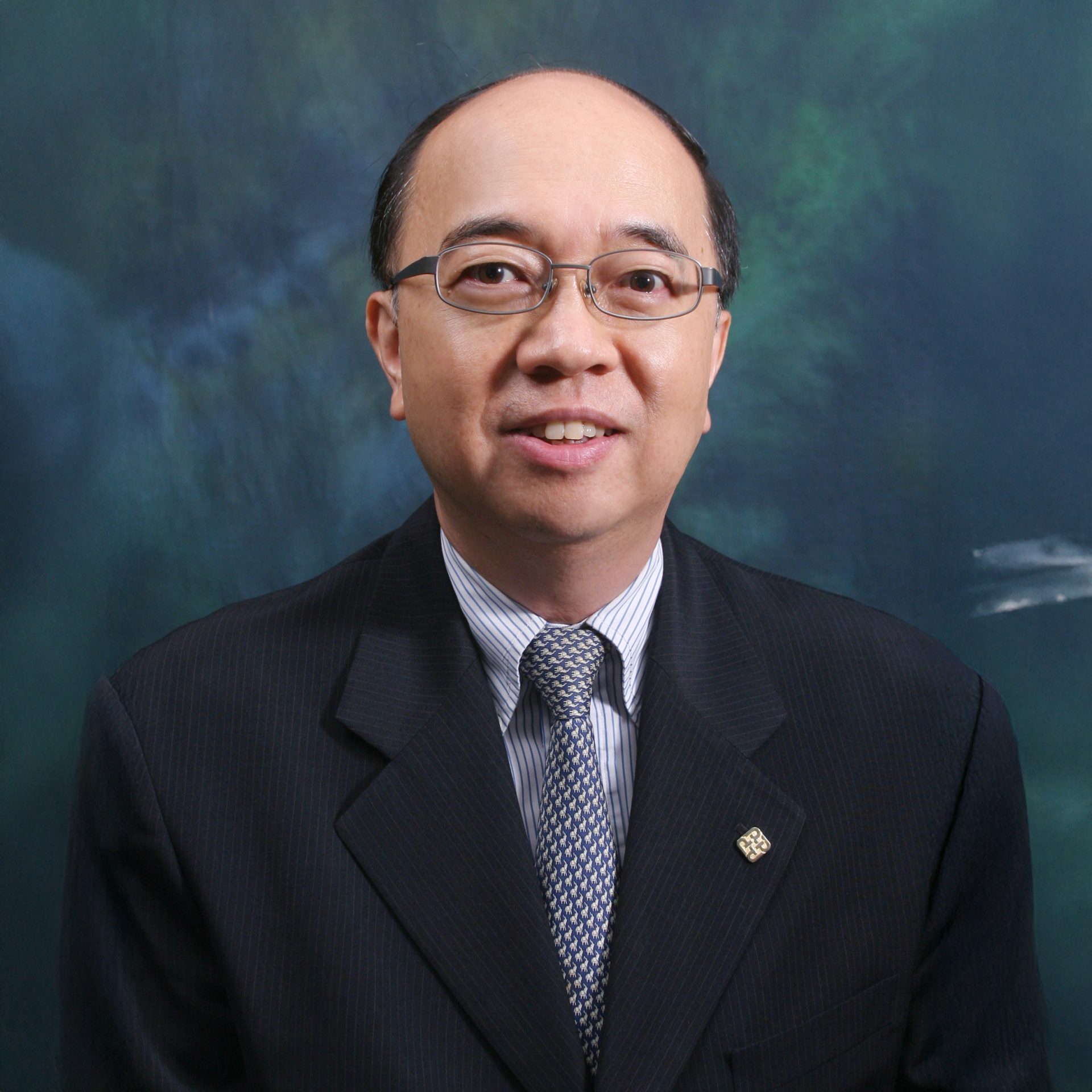 Professional headshot of a man wearing glasses, a suit, and patterned tie.