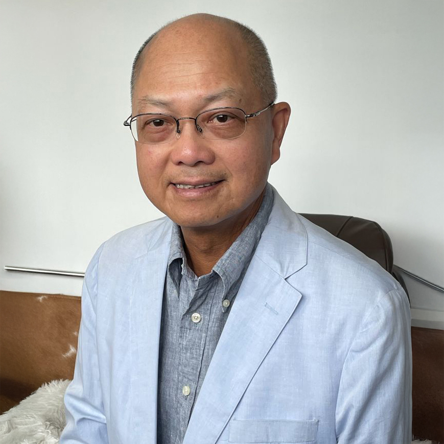 Portrait of a smiling man with glasses wearing a light blue blazer and gray shirt.