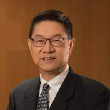 Portrait of a man wearing glasses, suit, and tie against a wooden background.