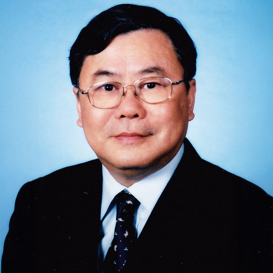 Portrait of a man wearing glasses, suit, and patterned tie against a blue background.