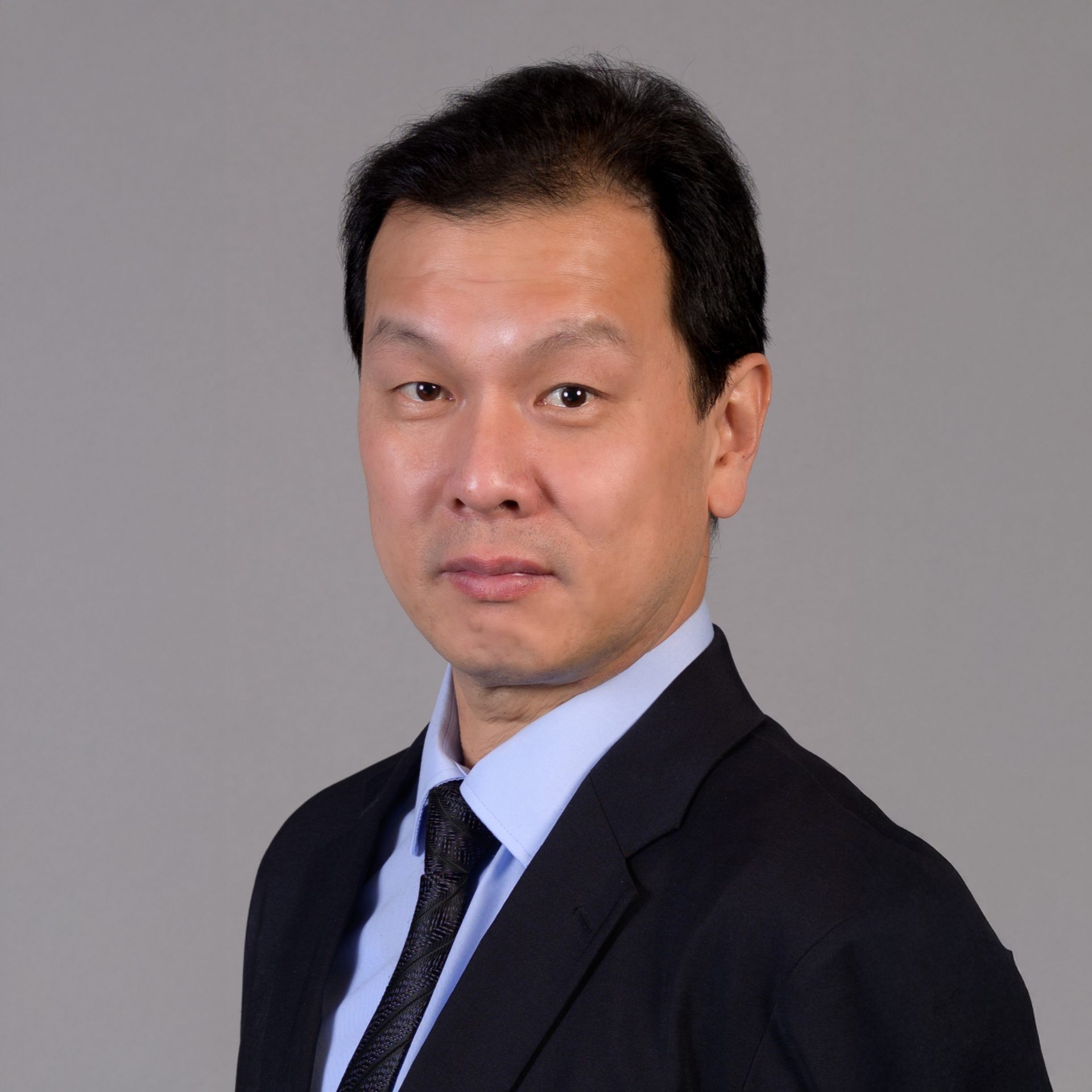 Professional headshot of a man in suit and tie against gray background