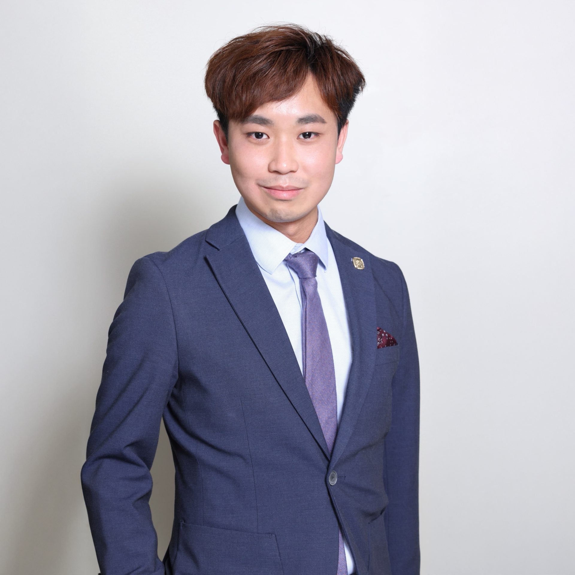Man in blue suit with purple tie and patterned pocket square, smiling at camera.