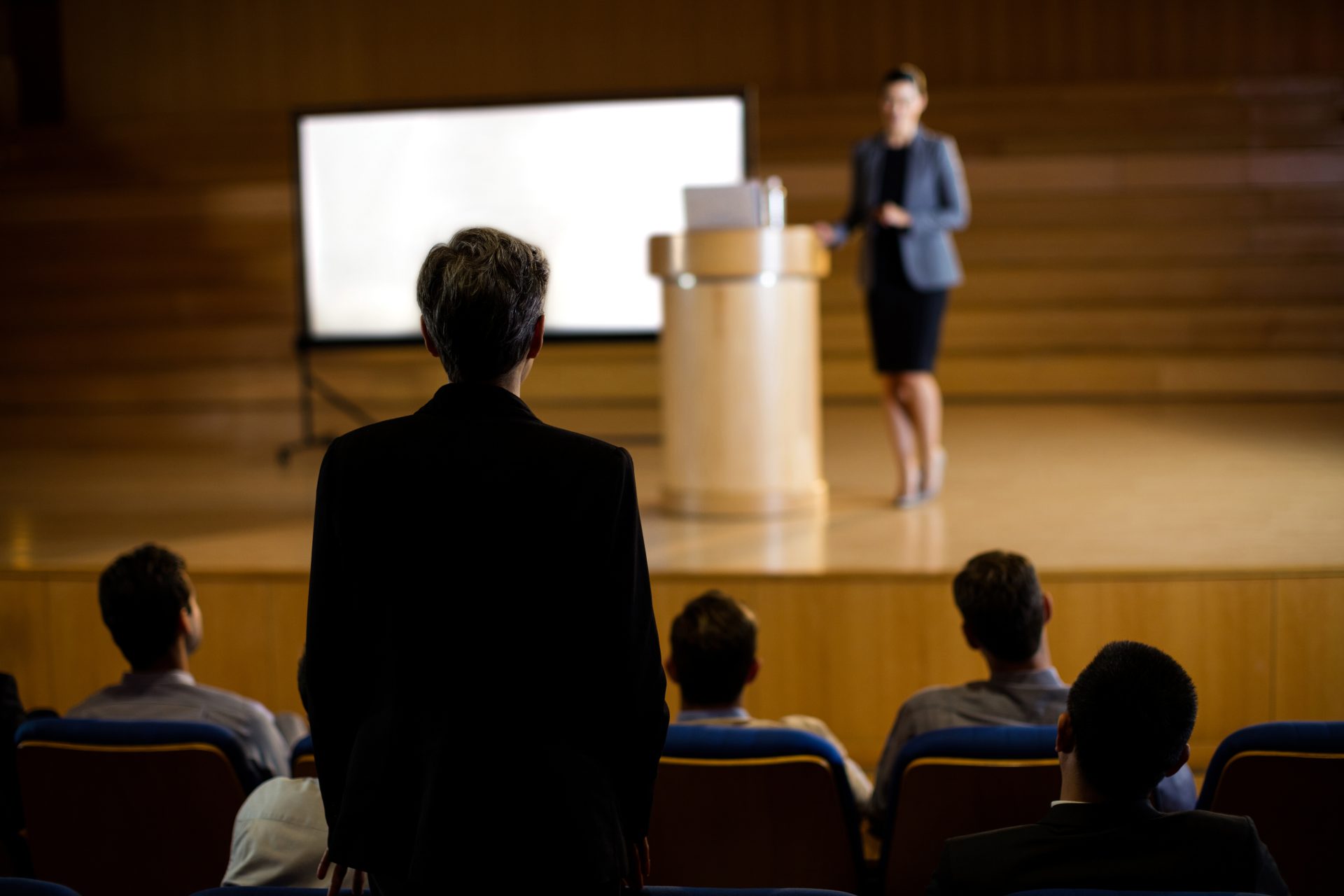 Female executive speaking at podium to audience in conference hall.