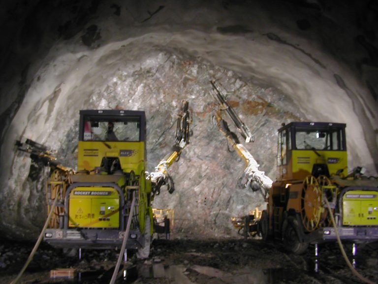 Two yellow tunnel boring machines operating in a dark underground mine tunnel.