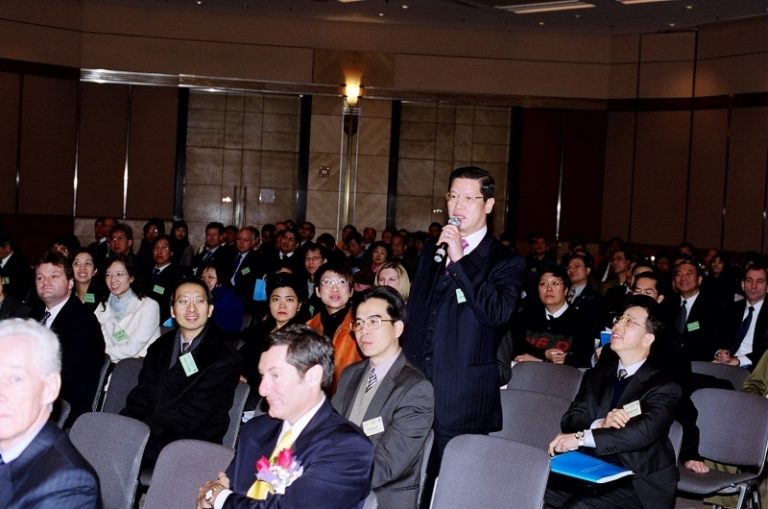 Man speaking into microphone at conference while audience listens attentively.
