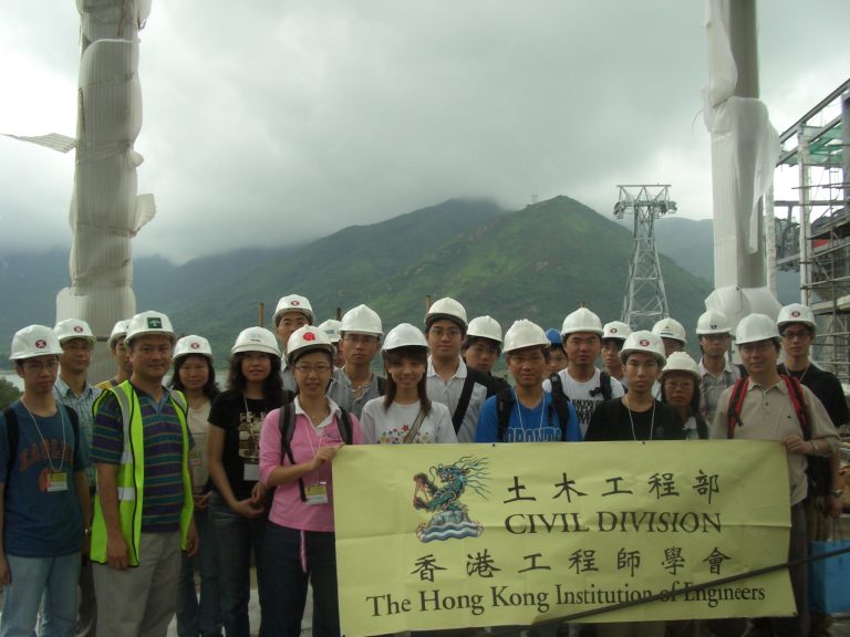 Group of civil engineering students in hard hats holding banner at construction site.