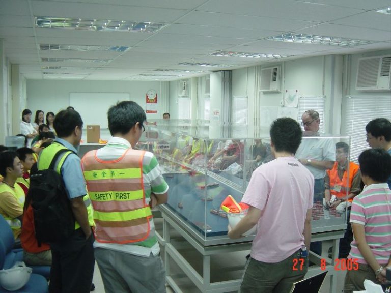 Group of people in safety vests observing a display case in an office setting.
