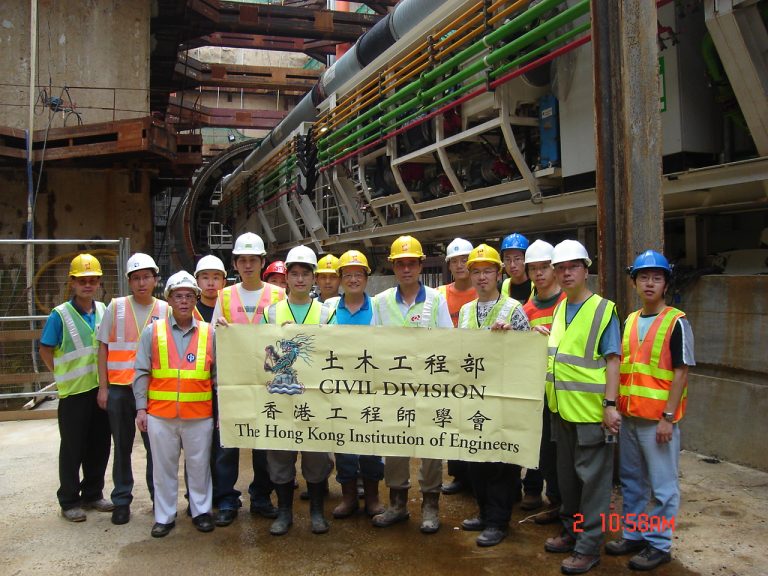 Civil engineers in safety gear pose with banner at construction site