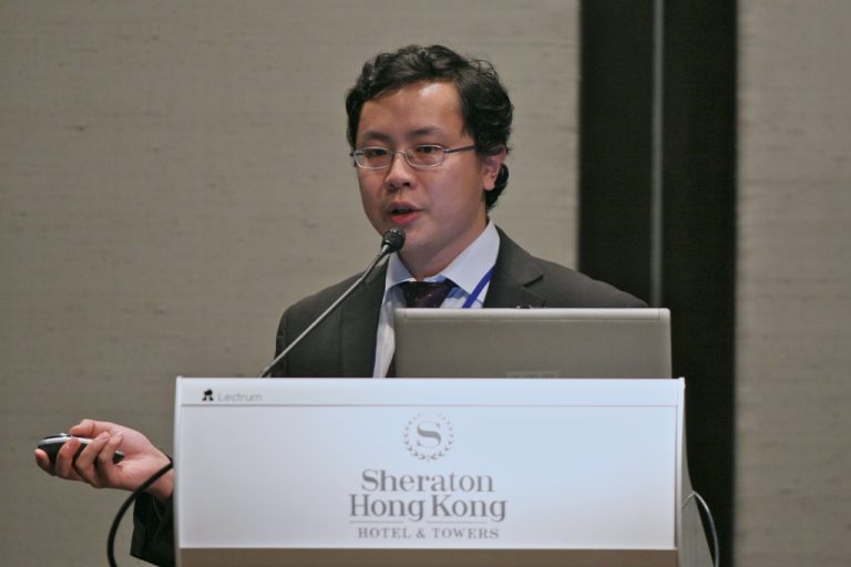 Man speaking at podium with laptop and mouse, Sheraton Hong Kong Hotel & Towers branding visible