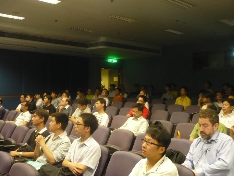 Audience seated in theater-style seating, attentively watching a presentation.