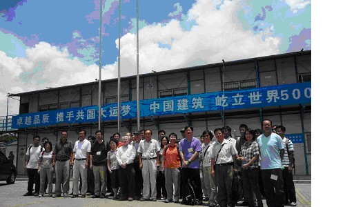 Group of people posing for photo in front of a large industrial building with Chinese signage.