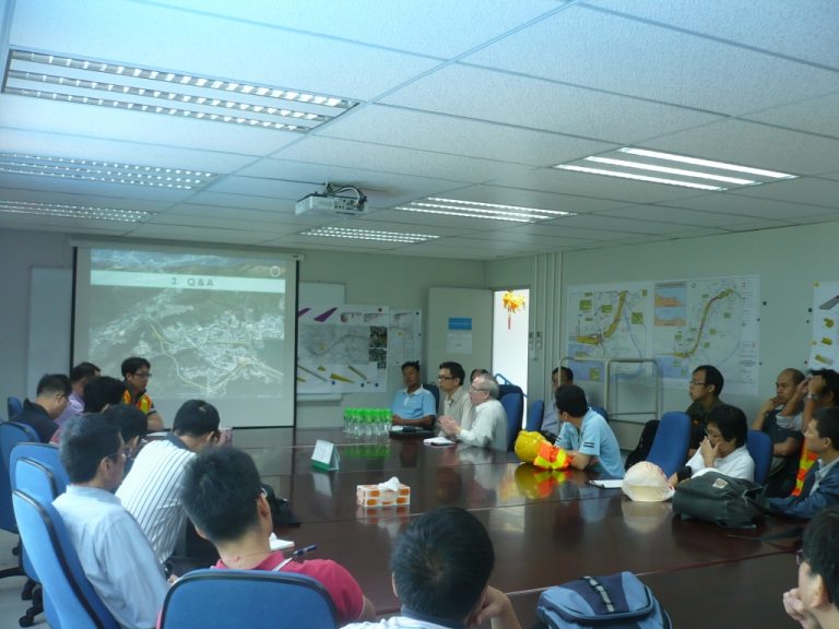 Group meeting in conference room with presentation on screen and maps on wall