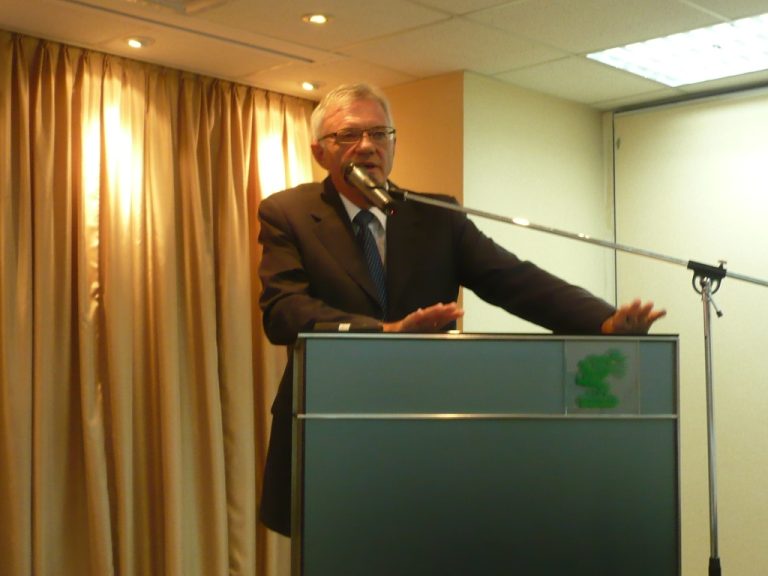 Man in suit speaking at podium with microphone and gesturing hands.