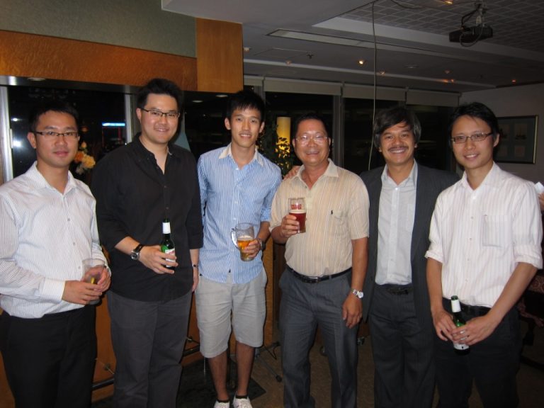 Six men posing together at a social gathering, holding drinks and smiling.