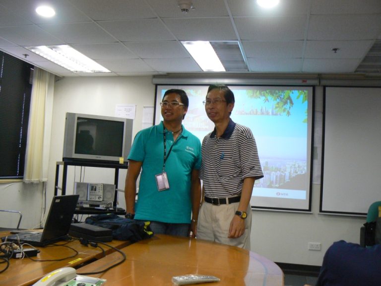 Two men standing in a conference room with a presentation screen behind them.